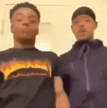 two young men are standing next to each other and looking at the camera in a room .