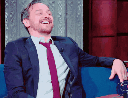 a man in a suit and tie laughs while sitting on a couch