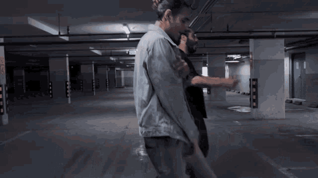 a man in a denim jacket is dancing in a dark parking garage