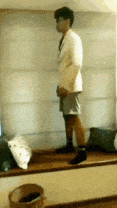 a man in a white jacket and shorts is standing on a window sill in a room .