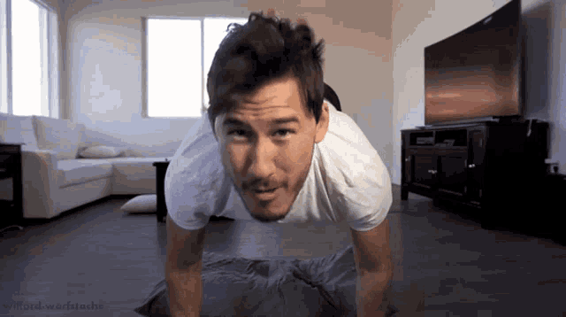 a man in a white shirt is doing push ups in a living room with a television in the background