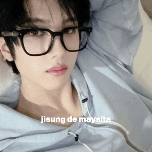 a young man wearing glasses and a light blue hoodie is laying on a bed