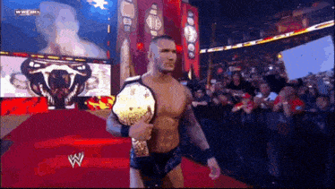 a wrestler is walking down a red carpet while holding a wrestling championship belt