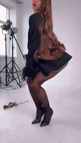a woman in a black dress and tights is standing in front of a rose