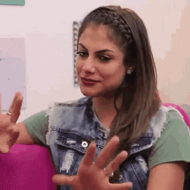 a woman wearing a denim vest and a green shirt is sitting on a pink couch with her hands outstretched