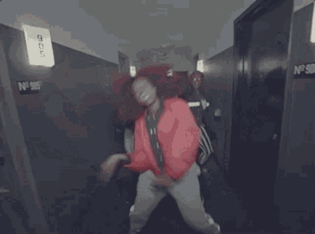 a woman in a red jacket is dancing in a hallway with a sign that says ' 104-105 '
