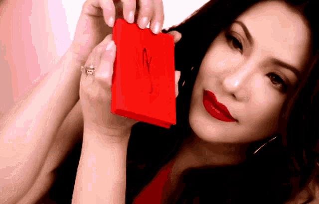 a woman with red lipstick is holding a small red box with the letter m on it