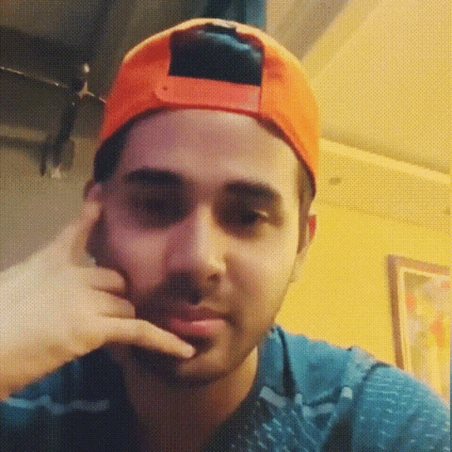 a man wearing an orange baseball cap holds his hand to his face