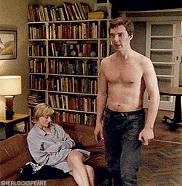a man without a shirt is standing next to a woman sitting on a couch in a living room