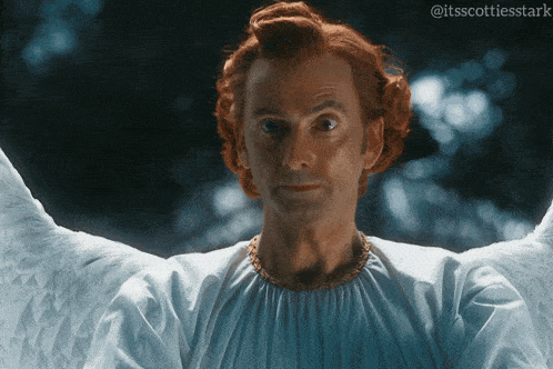 a man with red hair and white wings looks at the camera