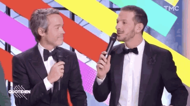 two men in tuxedos are holding microphones in front of a colorful background that says tmc on it