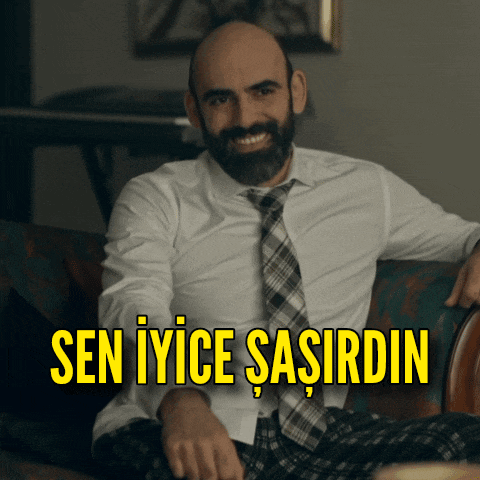 a man with a beard is sitting on a couch with the words sen iyice sasirdin above him