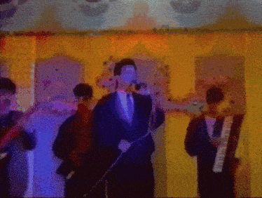 a man in a suit sings into a microphone while another man plays a keyboard
