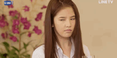 a young woman with long hair is making a funny face while sitting in front of a vase of flowers .