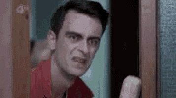 a man in a red shirt is standing in front of a door holding a piece of paper .