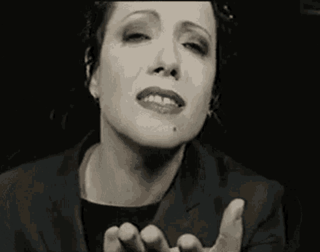 a woman in a black jacket is making a funny face with her hands outstretched in a black and white photo .