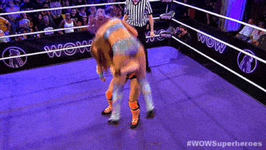 two women are wrestling in a ring with a wow banner in the background