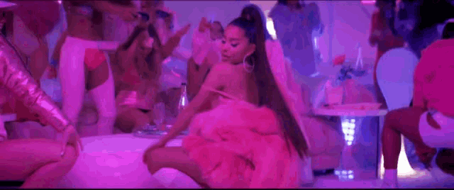 a woman in a pink dress is sitting on a table in a room surrounded by other women .
