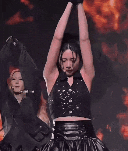 a woman in a black vest and skirt is dancing on stage with her arms in the air .