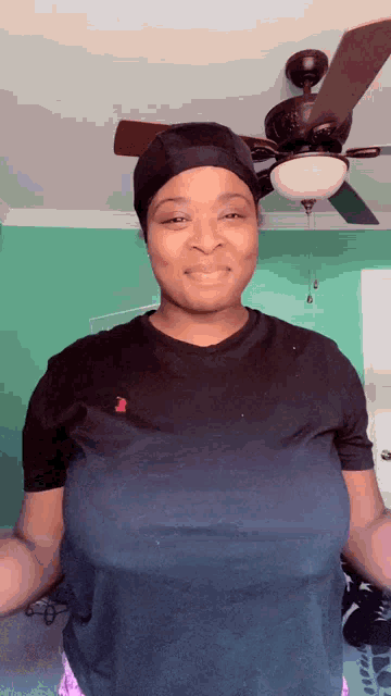 a woman wearing a black t-shirt and a hat is standing under a ceiling fan