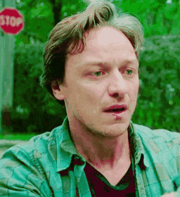 a man in a green shirt is standing in front of a red stop sign .