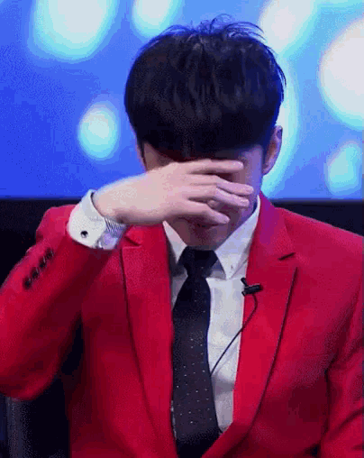 a man wearing a red suit and tie is covering his face with his hand .