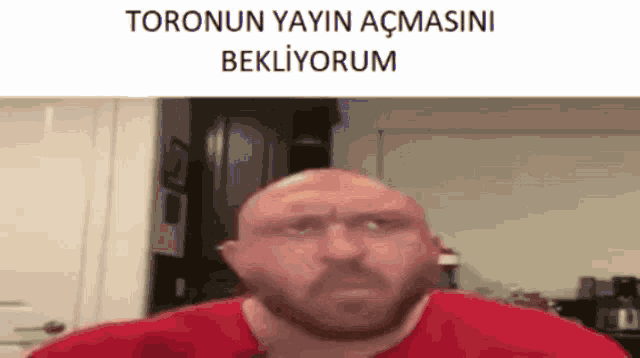 a bald man with a beard is wearing a red shirt and has the words toronun yayin acmasini bekliyorum written above him