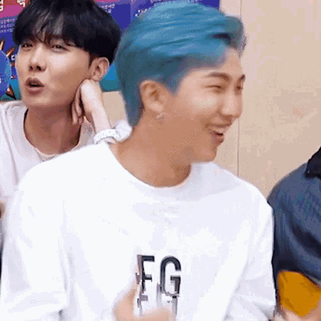 a man with blue hair is wearing a white shirt that says fg .