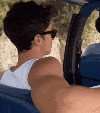 a man wearing sunglasses and a white tank top is driving a blue vehicle