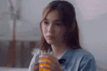 a girl is holding a glass of orange juice in her right hand
