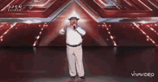 a man in a hat is singing into a microphone on a stage in front of an open beyond sign