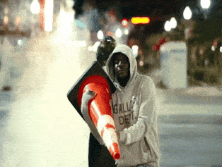 a man wearing a hoodie that says gallup det holds an orange cone