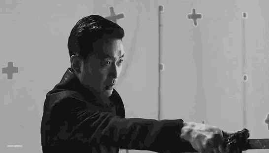 a man in a black coat is holding a sword in his hand in a black and white photo .