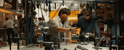 two men are working on a project in a workshop with a sign that says ' warning ' on it