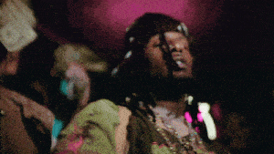 a man wearing a hat and a necklace has a dollar bill on his head