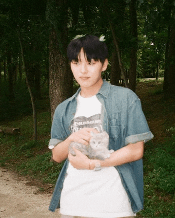 a young man in a denim shirt is holding a kitten in his hands