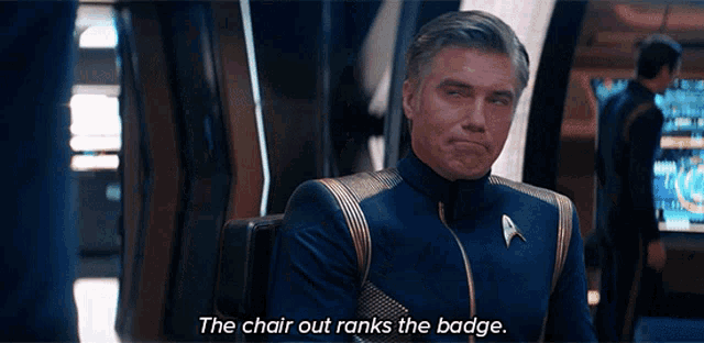 a man in a star trek uniform sits in a chair and says the chair out ranks the badge