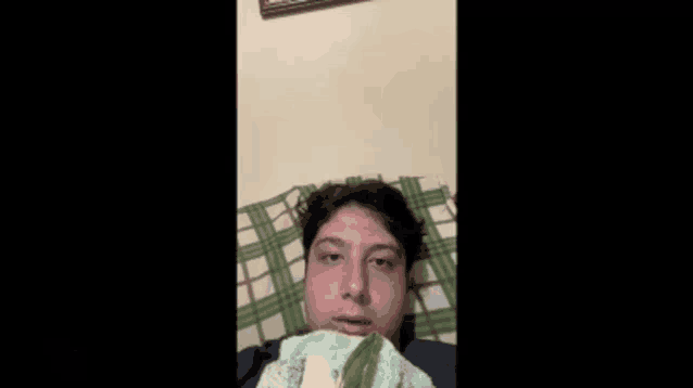 a young man is laying on a bed with a plaid blanket covering his head .