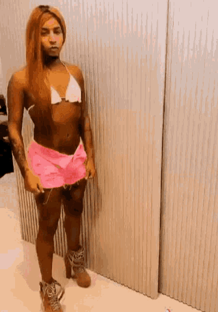 a woman is standing in front of a wall wearing a bikini top and pink shorts .