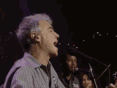 a man is singing into a microphone while another man plays a guitar .
