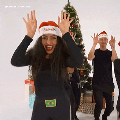 a woman wearing a santa hat is dancing in front of a christmas tree ..