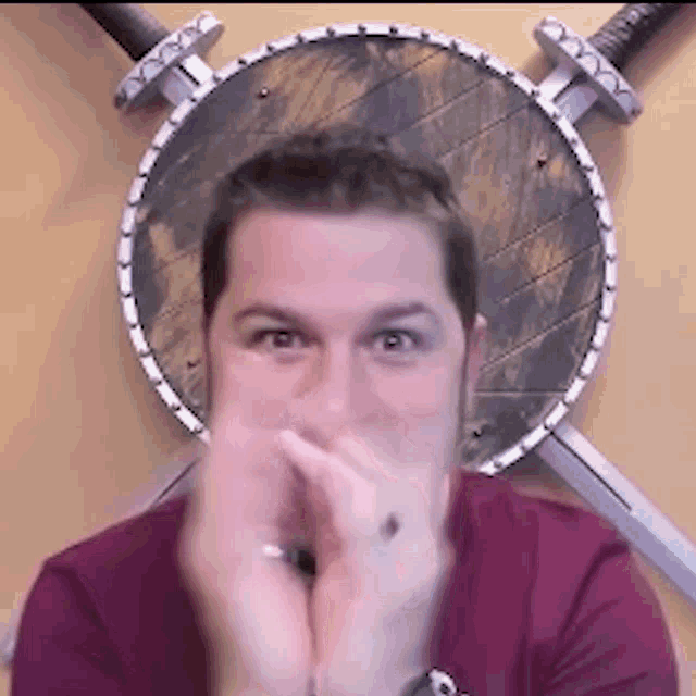 a man is covering his mouth in front of a shield and swords .