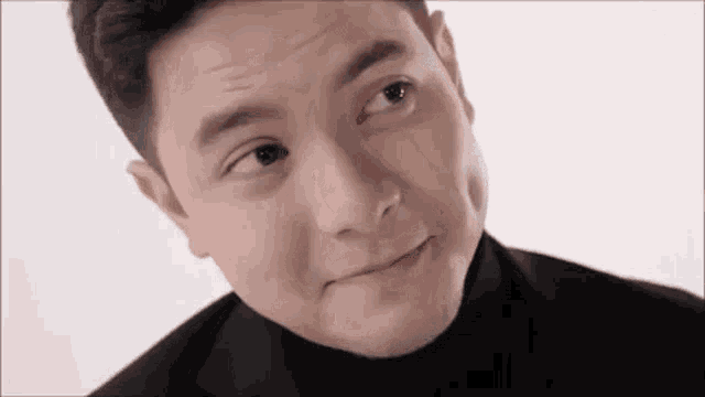 a close up of a man making a funny face while wearing a black suit and turtleneck .