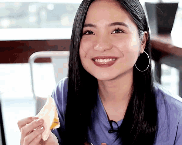 a woman wearing hoop earrings is smiling while holding a piece of bread