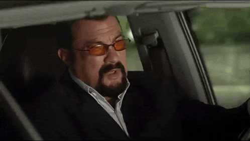 a man with a beard is sitting in a car wearing sunglasses .