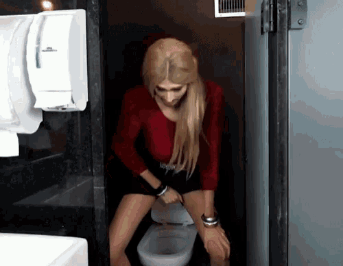 a woman sits on a toilet in a bathroom with a paper towel dispenser