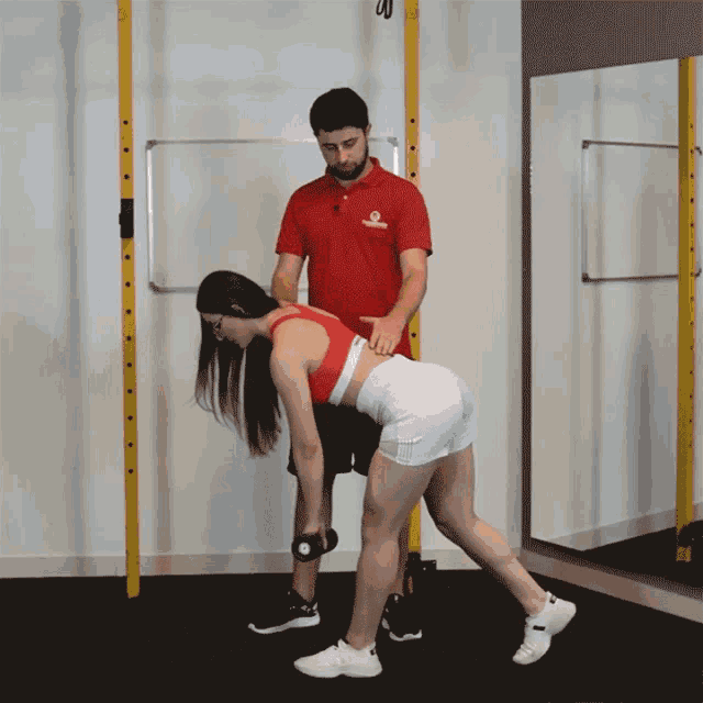 a man in a red shirt that says ' fitness ' on it is helping a woman lift weights