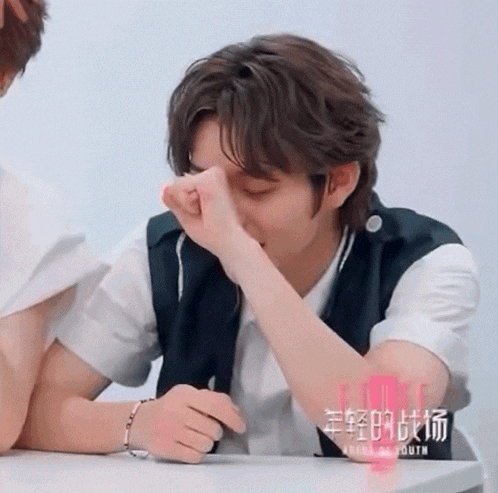 a young man sitting at a table with his hand on his face