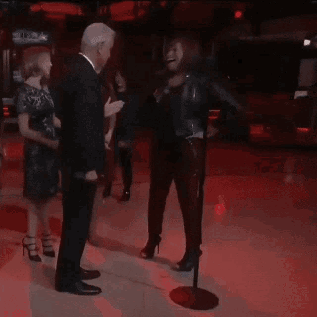 a man in a suit stands next to a woman in a black dress on a dance floor