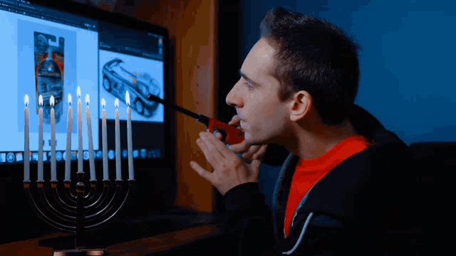 a man lighting candles on a menorah in front of a computer monitor